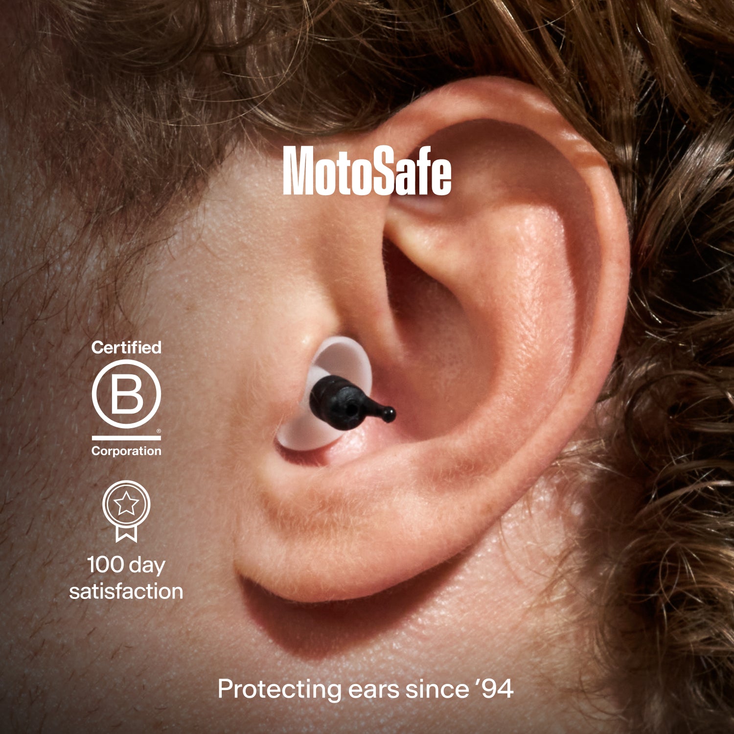 Close-up of an ear wearing an Alpine MotoSafe Tour earplug, with Certified B Corporation, "100 day satisfaction" and "Protecting ears since &