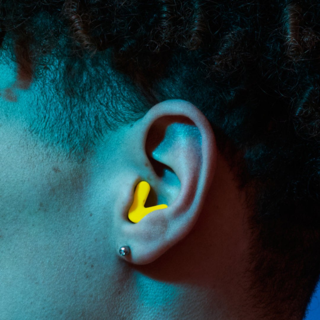 Detailed image of an ear with an Alpine Tune earplug in neon yellow showing the snug fit in ear 